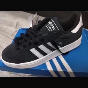 Svarta Adidas Campus sneakers - Snygga svarta Adidas Campus sneakers med vita detaljer och klassiska tre ränder på sidan. Skorna har en stilren design med snörning och en bekväm passform. Perfekta för en avslappnad stil.
