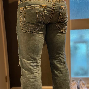 True religion unika jeans med slitningar. Väldigt sällsynta  - Snygga blå jeans från True Religion med slitningar och broderade bakfickor. De har en klassisk femficksdesign och en unik patch på baksidan. Perfekta för en avslappnad stil.. Aningen vida om man gillt det. Jag är 1,83 cl och är gammal hockey spelare så dom sitter okej på mig. Men lite tajt i midjan. Amerikansk storlek så jag skulle säga att dom är runt 33 i midjan och 34 i längd. Knappt använda och i stort sett omöjliga att få tag på. Även på den tiden då de såldes 