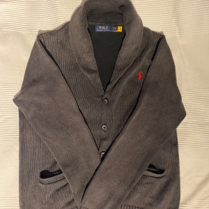 Grå cardigan från Polo Ralph Lauren - Säljer en stilren grå kofta från Polo Ralph Lauren med krage och knappar framtill. Skick 8/10 och storlek M kan passa S. Priset är inte hugget i sten och bara att skriva och fråga vid funderingar! 