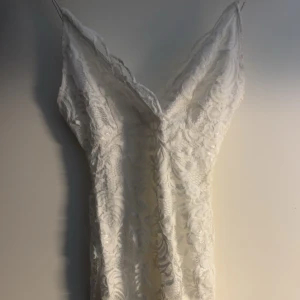 Vit spetsklänning Nelly - Elegant vit klänning med spetsdetaljer och v-ringad design. Perfekt för studenten. Använd 1 gång på min student. Går till knäna på mig och jag är 166 cm. Vid intresse så kan fler bilder skickas. ❤️‍🔥