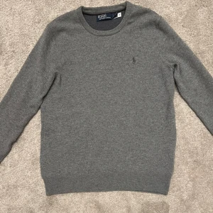 Grå tröja från Polo Ralph Lauren - Säljer en stilren grå tröja från Polo Ralph Lauren. Tröjan är långärmad och har en diskret logga på bröstet. Perfekt för en klassisk och avslappnad look. Nypris ~2000kr, storlek S, 100% ull. 