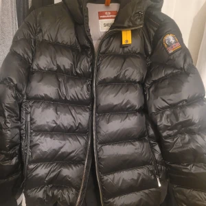Svart pufferjacka från Parajumpers - Pharrell - Svart - Snygg svart pufferjacka från Parajumpers med huva och dragkedja.  Perfekt för kyliga dagar. Köpt från johnells, använd 3 gånger. Kvitto bevis finns och även qr kod på jackan. Jätte bra skick, vill bli av med den då jag växt ur den. Nypris runt 3000