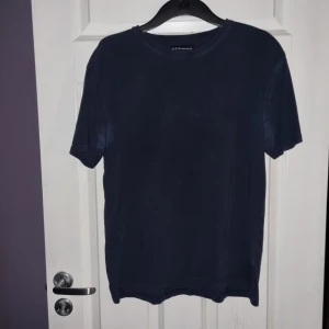 Mörkblå t-shirt från S.C.W - Säljer en stilren mörkblå t-shirt från S.C.W. Den har en klassisk rund hals och korta ärmar. Något sliten/missfärgad i armhålan,  är dock inte lika markant i verkligheten som på bilden.
