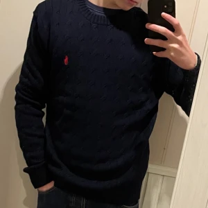 Mörkblå stickad kofta Polo Ralph Lauren - Säljer en snygg mörkblå stickad tröja från Polo Ralph Lauren med det klassiska röda logotypen på bröstet. Tröjan har en rund halsringning och långa ärmar, perfekt för kyligare dagar. Stor i storleken. Han på bilden är 175cm 💰 (Pris går att diskuteras vid snabb affär)💰 INGA RETURER!🚨