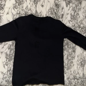 Svart långärmad tröja - Säljer en stilren svart långärmad tröja. Perfekt för kyligare dagar och enkel att matcha med olika outfits. Tröjan har en klassisk design utan extra detaljer.