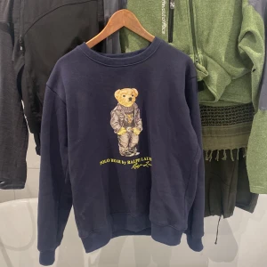 Mörkblå sweatshirt från Polo Ralph Lauren - Säljer en mörkblå sweatshirt från Polo Ralph Lauren med en ikonisk nallebjörn på framsidan. Tröjan har en rund halsringning och långa ärmar. Perfekt för en avslappnad stil. 🐻