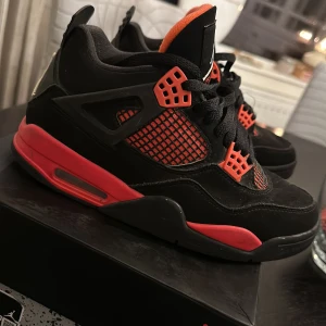Svarta och röda Nike Air Jordans 4 Storlek 40. I bra skick - Säljer ett par snygga Nike Air Jordans i svart och rött. Skorna har en cool design med snörning och den klassiska Jumpman-loggan på hälen. Perfekta för både vardag och fest! 🏀