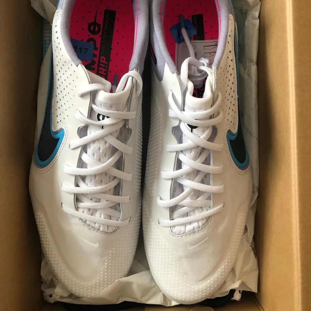 Säljer ett par Nike Tiempo fotbollsskor i vitt med snygga detaljer i turkos och rosa. Skorna har en klassisk snörning och är perfekta för fotbollsspel på gräs. De är i nytt skick.. Skor.