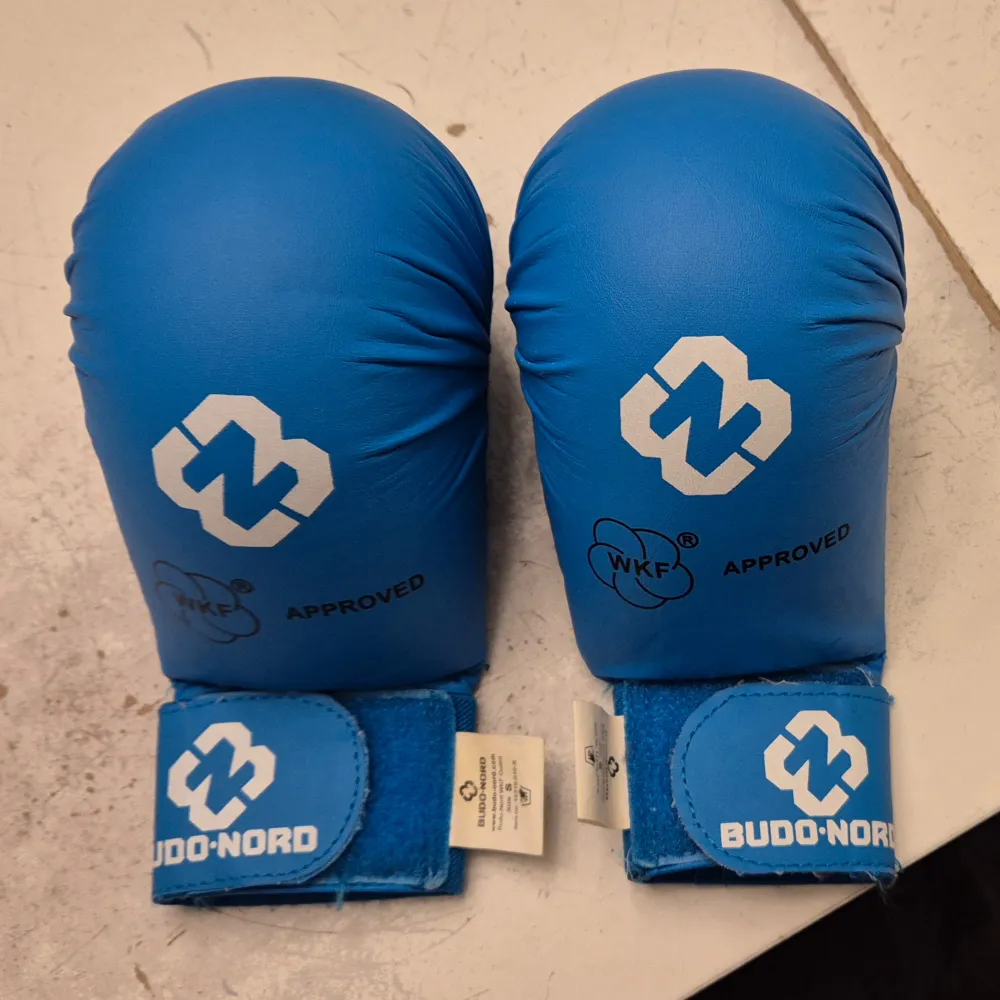 Säljer ett par blå kampsportshandskar från Budo-Nord i storlek S. De är WKF-godkända och har en justerbar kardborrestängning för perfekt passform. Perfekta för träning och tävling. Använda men i bra skick. Passa på att köpa dessa kvalitetsprodukter för din kampsportsträning! 🥊. Övrigt.