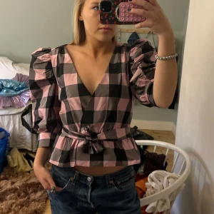 Rutig blus med puffärmar ifrån zara - Säljer en superfin rutig blus i rosa och svart med puffiga trekvartsärmar och v-ringning. Blusen har en omlott-design och ett knytband i midjan som ger en snygg passform. Går att knyta fram och bak✨✨✨