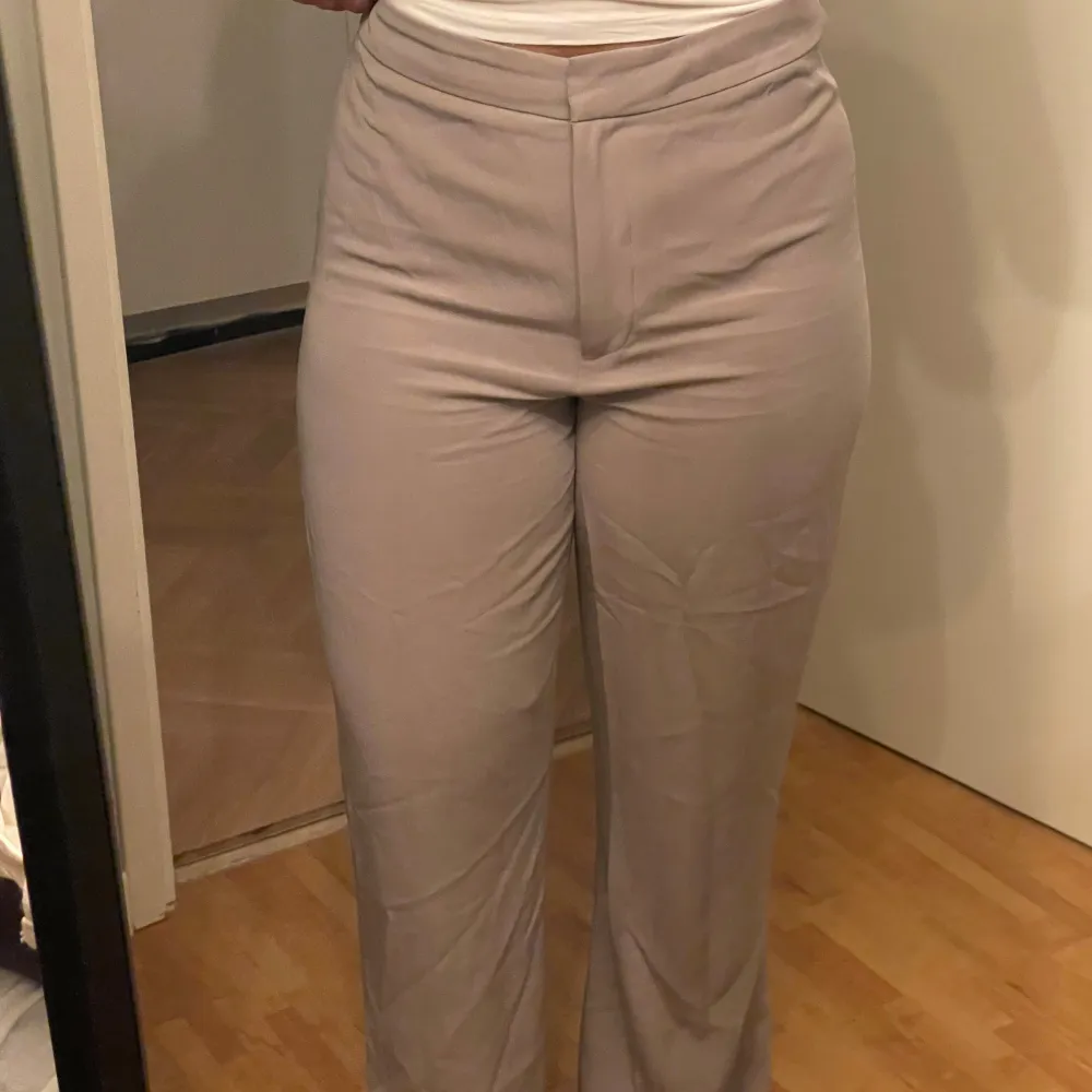Säljer ett par stilrena beige kostymbyxor i mycket bra skick. De är högmidjade och har en straight passform som ger en klassisk look. Perfekta för både kontoret och mer formella tillfällen. Materialet är super mjukt och bekvämt mot huden. Säljer då dem tyvärr är för stora/för långa för mig.. Farkut & Housut.