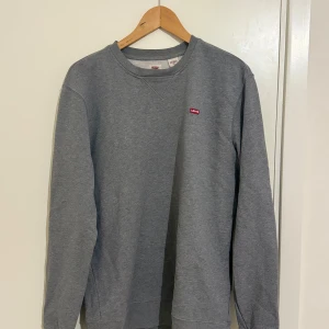 Grå sweatshirt från Levi's - Säljer en klassisk grå sweatshirt från Levi's i storlek M. Tröjan är i mycket bra skick och har en liten röd Levi's-logga på bröstet. Perfekt för både höst och vår, med långa ärmar och en bekväm passform. Perfekt för vardagsbruk eller en avslappnad stil.