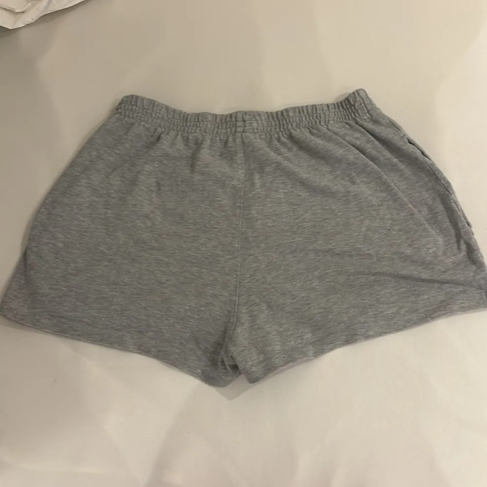 Säljer ett par grå shorts från Brandy Melville i mjukt bomullsmaterial. De har en elastisk midja och en liten slits på sidorna för extra komfort. På framsidan finns ett broderat märke med texten 'St. George London'. Perfekta för en avslappnad dag eller träning!. Shorts.