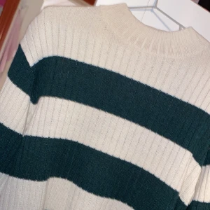 Randig stickad tröja från H&M - Säljer en supermysig stickad tröja från H&M i storlek 170. Den har breda ränder i beige och mörkgrön, perfekt för höst och vinter. Tröjan är långärmad och har en ribbad struktur som ger en skön passform. Perfekt för att hålla sig varm! 🍂Den är oanvänd. Jag fick den för nån dag sedan men det är inte direkt min stil. Vill inte slänga den därför säljer jag den.