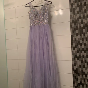 Ljuslila lång balklänning med paljetter i storlek XS/S - Säljer en fantastisk ljuslila lång balklänning med glittrande paljetter på överdelen. Klänningen har en v-ringad design och är ärmlös, perfekt för bal eller fest. Den flytande kjolen ger en drömlik känsla. Perfekt för att glänsa på speciella tillfällen!