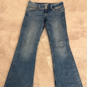 Blå bootcut jeans från Gina tricot  - Säljer ett par snygga blå lågmidjade bootcut jeans från Gina tricot i storlek 146 (passar även den som bär strlk 152). De har en klassisk femficksdesign med dubbla knappar i midjan och är i väldigt bra skick. Perfekta för både vardag och fest!