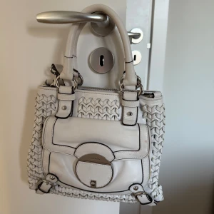 Vit handväska från Karen Millen - Säljer en superfin vit handväska från Karen Millen. Den har ett snyggt flätat mönster och en praktisk ficka framtill med ett stilrent spänne. Perfekt för både vardag och fest! 👜✨ny pris 1550kr