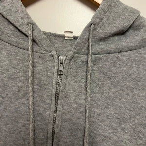 Grå hoodie med dragkedja - Säljer en grå hoodie i mjukt material med dragkedja framtill. Den har en bekväm passform och är perfekt för vardagsbruk. Huvan har dragsnören och det finns praktiska fickor på framsidan. Perfekt för kyliga dagar! Pris kan diskuteras!!💓