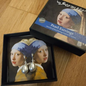 Silverfärgade pärlörhängen inspirerade av Vermeer - Säljer ett par eleganta silverfärgade pärlörhängen inspirerade av Vermeers konstverk. De har en klassisk droppform och kommer i en fin presentförpackning. Perfekta för att ge en touch av tidlös elegans till din outfit.