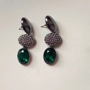 Eleganta örhängen med gröna stenar - Snygga örhängen med en glamorös look! De har en stor grön oval sten längst ner, en glittrig sektion i mitten och en mörk, glänsande topp. Perfekta för en fest eller en speciell kväll. De mäter cirka 6 cm i längd och är i nyskick. Lägg till lite bling i din outfit! ✨