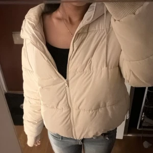 Beige pufferjacka - Säljer en snygg beige pufferjacka med dragkedja och huva. Jackan är perfekt för kyliga dagar och har en skön, vadderad känsla. Den är långärmad och passar bra till både vardag och lite finare tillfällen. Perfekt för höst och vinter!