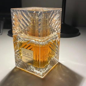 Khamrah parfym från Lattafa - Säljer en lyxig Khamrah parfym från Lattafa. Flaskan är fyrkantig med ett elegant mönster och gyllene detaljer. Parfymen har en varm, bärnstensfärgad vätska som ger en känsla av exklusivitet. Perfekt för speciella tillfällen eller som en fin present.