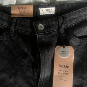 Svarta byxor från Lindex - Säljer ett par svarta byxor från Lindex i modellen Jackie. De är högmidjade med en wide leg-stil, vilket ger en snygg och modern look. Byxorna är gjorda av ekologisk bomull, vilket gör dem både bekväma och hållbara. Perfekta för både vardag och fest! Sitter jätte fint i rumpan och är mina favorit byxor men är tyvärr för små! Priset går att diskutera