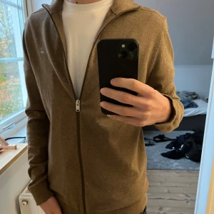Brun kofta från Selected Homme - Säljer en snygg brun kofta från Selected Homme i storlek S. Den har en dragkedja framtill och är perfekt för höst. Materialet är mjukt och bekvämt, perfekt för lager-på-lager-stil. Passar både till vardags och lite mer uppklädda tillfällen.