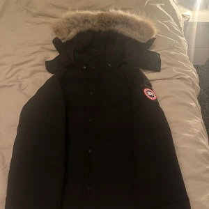 Svart dunjacka från Canada Goose - Säljer en svart Canada Goose dunjacka i mycket bra skick. Den har en stor, fluffig pälsfodrad huva och är perfekt för kalla vinterdagar. Jackan är använd 2-3 gånger men inte min stil längre.