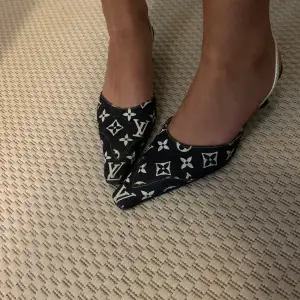 Snygga svarta pumps med vit monogramdesign. De har en spetsig tå och en elegant klack. Perfekta för en stilren look på festen eller middagen. Skorna har en bekväm passform med en smal rem runt hälen.