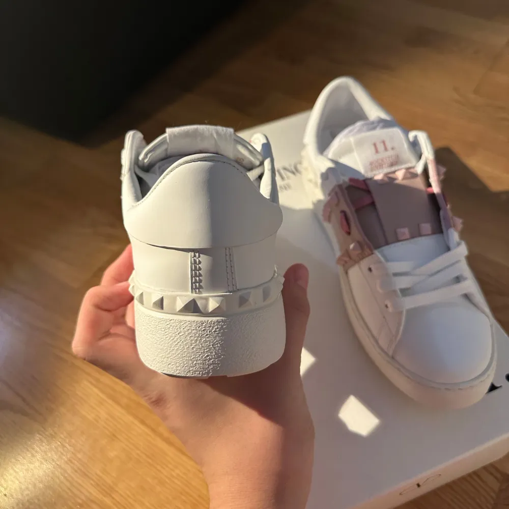 Säljer ett par snygga Valentino Rockstud sneakers i vitt skinn med rosa detaljer. Skorna har de ikoniska nitarna på sidorna och en bekväm passform. Perfekta för att ge din outfit en lyxig touch. Aldrig använda! Priset går att ändra på. Skor.