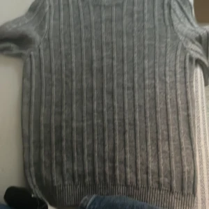 Grå ribbad tröja från Qustyle - Säljer en snygg grå ribbad tröja från Qustyle. Perfekt för kyliga dagar med sin mjuka och bekväma passform. Tröjan har långa ärmar och en klassisk rund halsringning. Passar både till vardags och lite finare tillfällen. 🩶