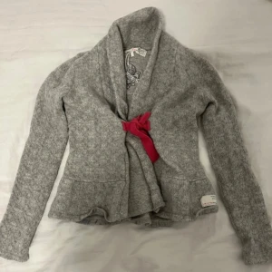 Grå kofta från Odd Molly - Mysig grå kofta från Odd Molly med en rosa rosett framtill. storlek S men väldigt liten i storlken så passar bättre åt xs hållet skulle ja säga, köpt på sellpy o har kvar sellpy prislappen💗