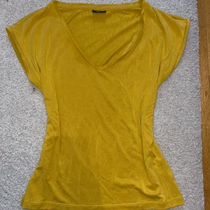 Gul v-ringad topp från Pieces - Säljer en solgul v-ringad topp från Pieces. Den har en enkel och stilren design med korta ärmar och en figurnära passform. Knappt använd och i nyskick.