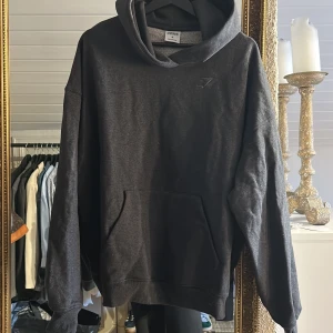 Mörkgrå hoodie från Gymshark - Säljer en stilren mörkgrå hoodie från Gymshark. Den har en klassisk design med en känguruficka framtill och en diskret logga på bröstet. Perfekt för en avslappnad look. HELT NY 