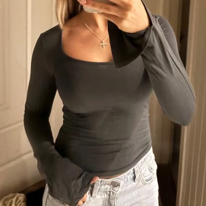 Svart långärmad topp - Snygg svart långärmad topp med en fyrkantig ringning. Perfekt för en stilren look och kan enkelt matchas med olika outfits. Toppen har en tight passform och är tillverkad i ett mjukt material.