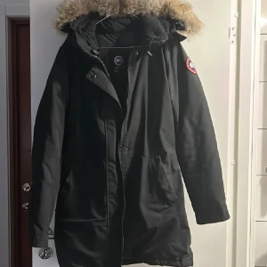 Svart parkajacka från Canada Goose - Säljer en svart parkajacka från Canada Goose med pälsfodrad huva. Jackan har dragkedja och knappar framtill samt två stora fickor. Perfekt för kalla vinterdagar. Finns i Stockholm. 