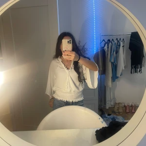 Vit blus från NLY Design - Säljer en vit blus från NLY Design med v-ringning och knytning framtill. Blusen har vida ärmar och en smockdetalj vid midjan som ger en fin passform. Perfekt för en stilren look.