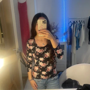 Svart blommig topp - Säljer en svart topp med vackert blommönster i rosa och vita nyanser. Toppen har trekvartsärmar och en rund halsringning. Perfekt för en stilren och romantisk look.