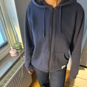 Mörkblå hoodie med dragkedja - Säljer en mörkblå hoodie med dragkedja och huva. Tröjan har långa ärmar och praktiska fickor framtill. Perfekt för en avslappnad stil.