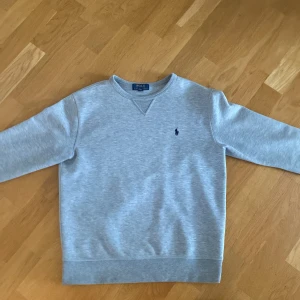 Grå tröja från Polo Ralph Lauren - Säljer en grå övertröja från ralph lauren. Tröjan är storlek L i barn och passar perfekt för dig som är runt 170 lång!