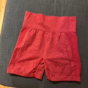Röda träningsshorts med hög midja - Snygga röda träningsshorts från Xshapes. Storlek L men passar M-L skulle jag säga. Bra skick. OBS! ”Hålen” är en del av modellen & inget som är trasigt. Ingen scrunch men konturer bak som framhöver rumpan. 