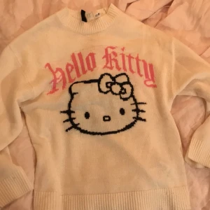 Vit Hello Kitty tröja från H&M Divided - Säljer en söt vit tröja från H&M Divided med Hello Kitty-motiv i svart och rosa text. Tröjan har långa ärmar och en rund halsringning. Säljer då den inte används. Har en liten fläck nära rosetten, kolla min bio för mer info💗