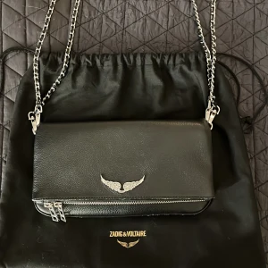Svart axelväska Zadig & Voltaire -  Hej, intresse koll på min Zadig & Voltaire väska i skinn, med silverdetaljer och kedjerem. Väskan är i fint skick, men har små defekter längst ner på kanten, som knappt syns. Den är inköpt 2022 men är väl omhändertagen. Den kommer tyvärr inte till användning längre. Pris är inte hugget i sten, går att diskutera! Bara att höra av sig vid frågor eller fler bilder! 🥰 