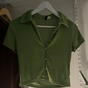 Grön kortärmad topp med knappar - Snygg grön kortärmad topp med knappar framtill och klassisk krage. Perfekt för en avslappnad stil.