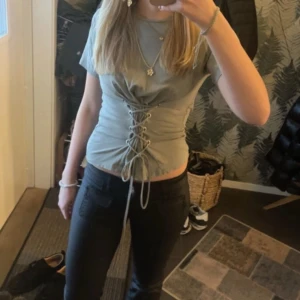 Grön topp med snörning från New Look - Snygg grön topp från New Look med snörning framtill som ger en cool look. Toppen har korta ärmar och en figurnära passform. Perfekt för att ge din outfit en extra touch.