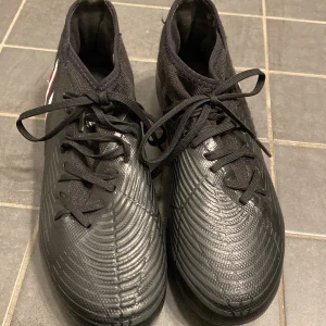Svarta fotbollsskor från Adidas nya  - Snygga svarta fotbollsskor från Adidas med blå och vita detaljer. Skorna har snörning och en slitstark sula med blå dobbar för bra grepp på planen. Perfekta för fotbollsträning och matcher.