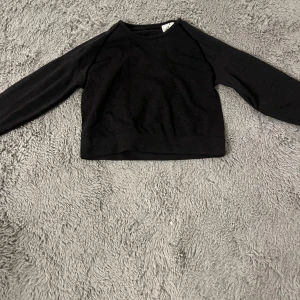 Svart tröja med långa ärmar - Säljer en stilren svart tröja med långa ärmar. Den är kort och passar perfekt för träning. Tröjan har en enkel design och är gjord i ett mjukt material.