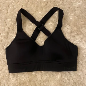 Svart sport-bh med korsade band - Säljer en svart sport-bh med korsade band i ryggen. Den har justerbara hakar för perfekt passform och är tillverkad i ett mjukt, stretchigt material.