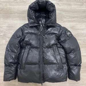 Canada Goose Crofton puffer - Snygg svart pufferjacka från Canada Goose black label med hög krage och dragkedja. Jackan har en broderad logotyp på ärmen och är perfekt för kalla dagar. Helt ny i Strl S. 